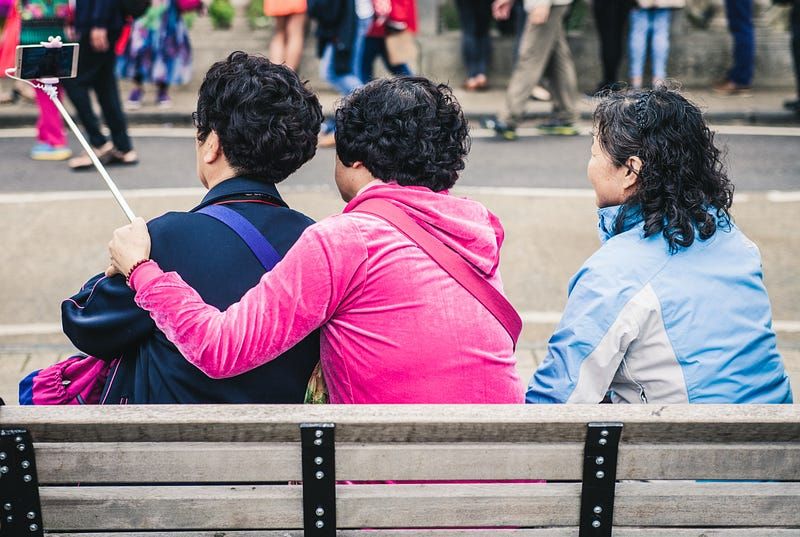 Three people sitting on a bench and taking a selfie together.