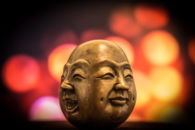 An image of a carved egg shaped sculpture with a happy and neutral face on each side.